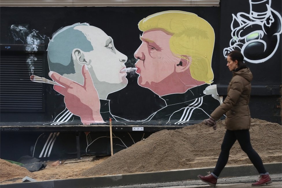 Женщина проходит мимо фрески, на которой избранный президент США Дональд Трамп (справа) выпускает дым марихуаны в рот президента России Владимира Путина на стене ресторана 23 ноября 2016 года в Вильнюсе, Литва.