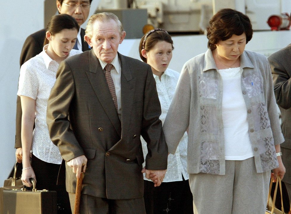 Хитоми ведет своего хилого мужа за руку, пока их дочери идут позади в международном аэропорту Токио 18 июля 2004 г.
