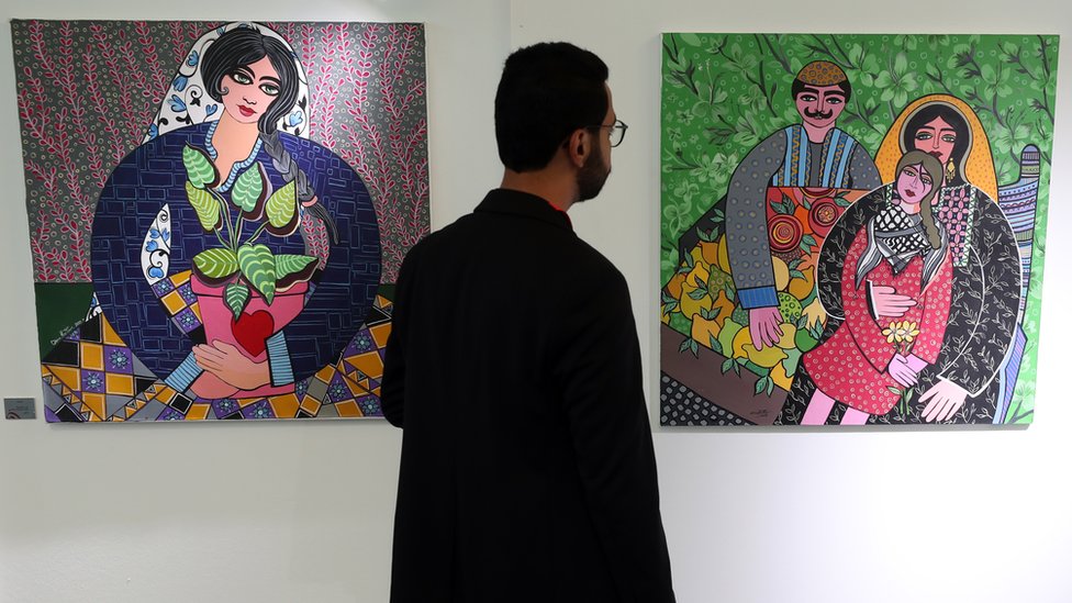 رجل يقف بين لوحتين في معرض (على اليسار لوحة لامرأة، وعلى اليمين لوحة لرجل وامرأة وطفل) في تونس العاصمة، تونس - السبت 27 مايو/ أيار 2023