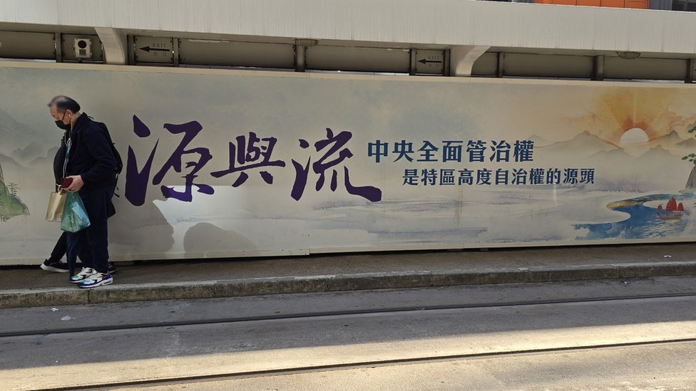 香港北角某電車站一位乘客走過宣傳中國對香港「全面管治權」的大型廣告（BBC中文圖片12/3/2024）
