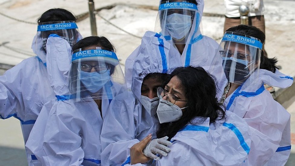 A group of medical workers in full PPE hug each other.
