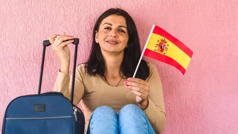 Mulher com bandeira da Espanha e mala de viagem