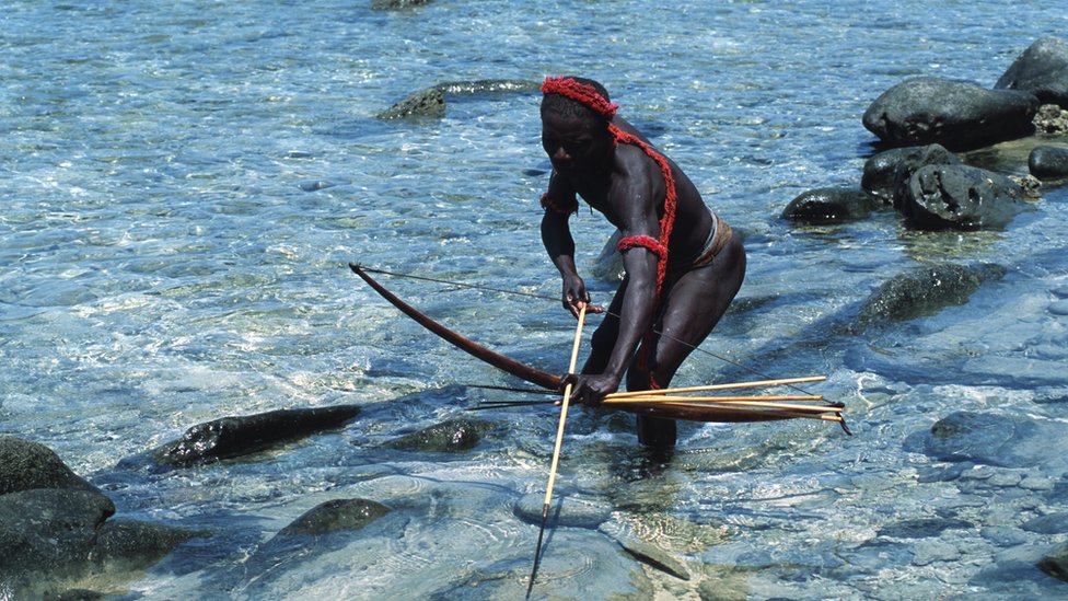   Un hombre jarawa de pie en el agua con un arco y una flecha. 