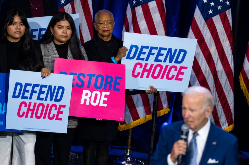 Tres mujeres sostienen carteles mientras el presidente Joe Biden habla de la importancia del derecho al aborto en un evento auspiciado por el Comité Nacional Demócrata en el Howard Theatre de Washington, D.C. el 18 de octubre de 2022.