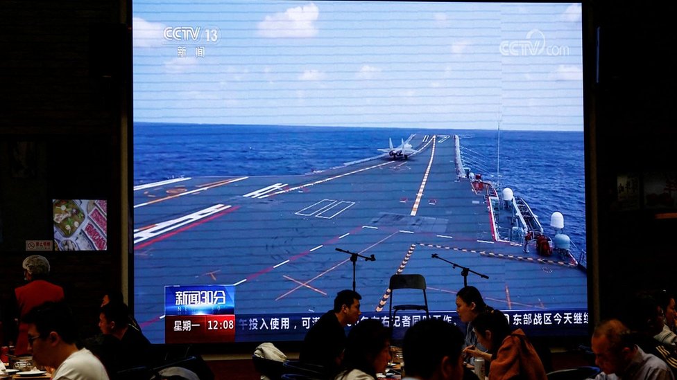 FILE PHOTO: Customers dine near a giant screen broadcasting news footage of an aircraft taking off from China"s Shandong aircraft carrier while taking part in a combat readiness patrol and "Joint Sword" exercises around Taiwan conducted by the Eastern Theatre Command of China"s People"s Liberation Army (PLA), at a restaurant in Beijing, China April 10, 2023.