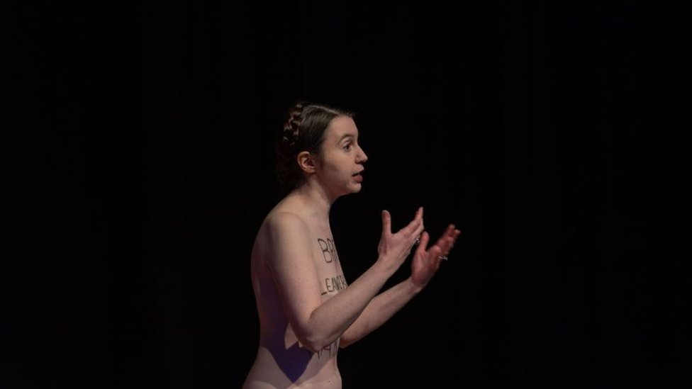 Dr Victoria Bateman giving a talk standing naked