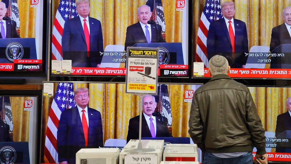 Израильтянин смотрит телевизионную пресс-конференцию президента США Дональда Трампа и премьер-министра Израиля Биньямина Нетаньяху в магазине электроники в израильском городе Модиин
