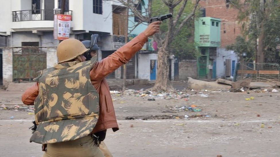Полицейский направляет пистолет в сторону протестующих во время демонстраций против нового закона Индии о гражданстве в Канпуре