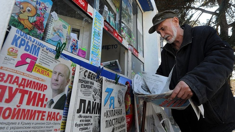 A man looks through a newspaper at a kiosk with Russian newspapers displayed outside in the Crimean port of Sevastopol on March 27, 2014.