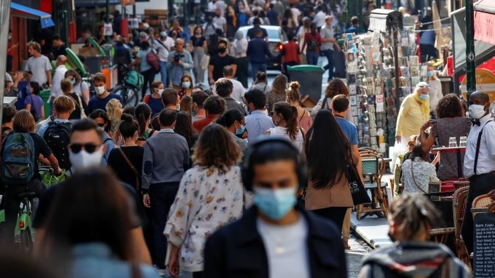 People wear masks while walking along a busy Paris street