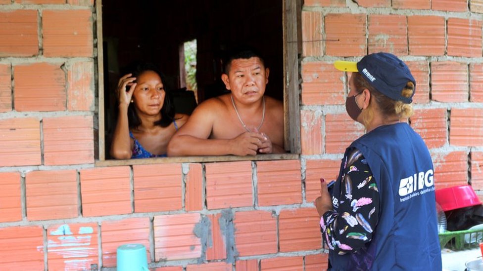 Recenseador entrevsitando homem e mulher através de janela em casa de tijolos aparentes