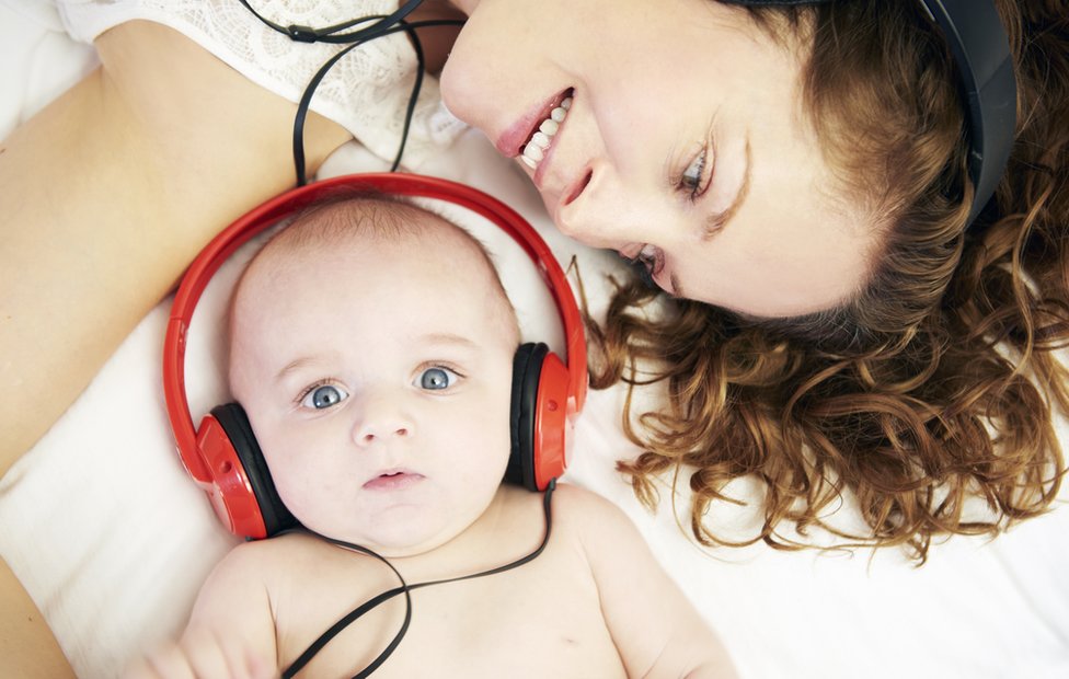 Bebê com fones de ouvido ao lado de sua mãe