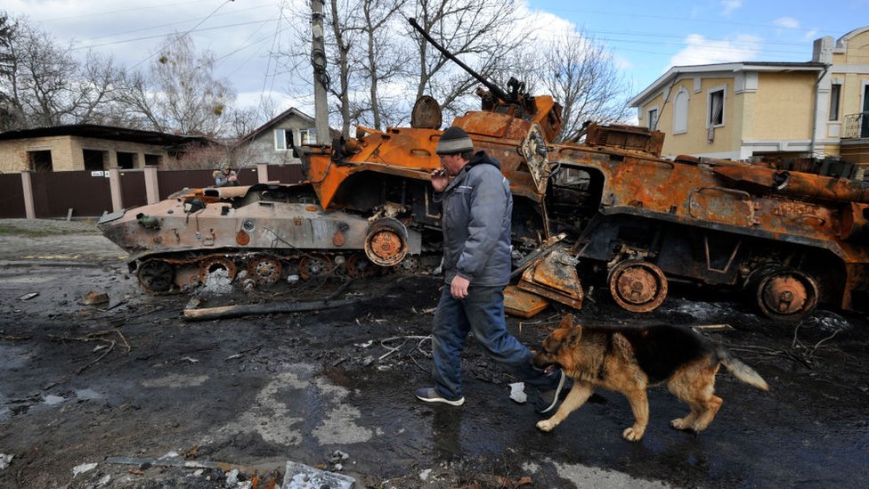 Un hombre camina con su perro junto a un tanque ruso destruido en Ucrania.