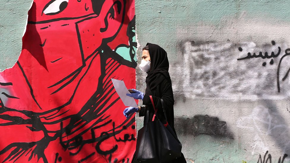 Woman walks past graffiti in Tehran