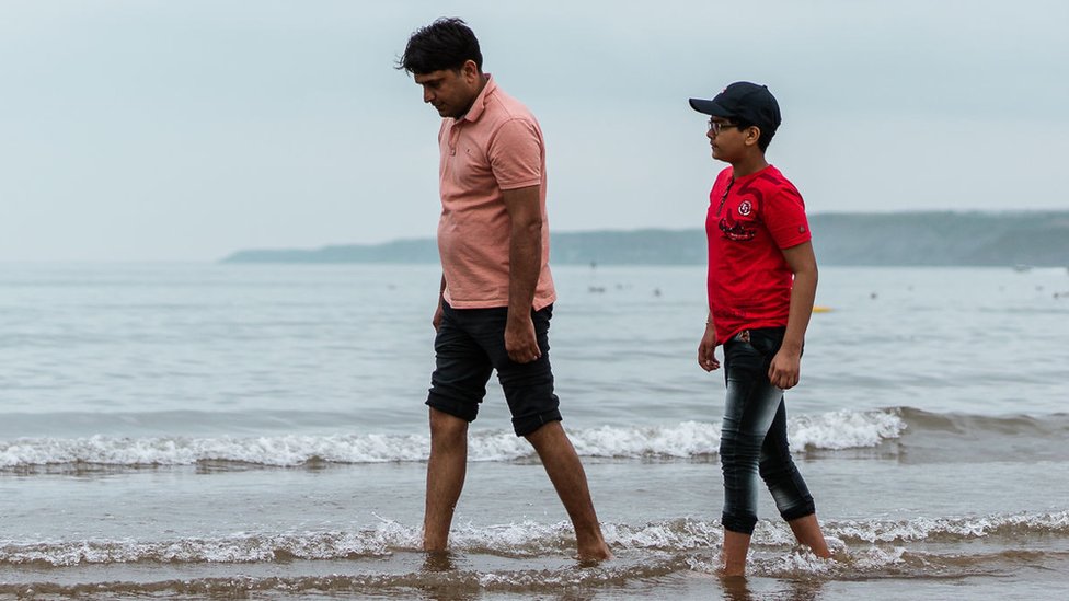 Отец и сын гуляют по пляжу, у их ног плещется вода