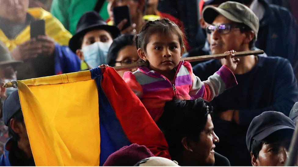 Una niña con una bandera de Ecuador junto a otras personas.