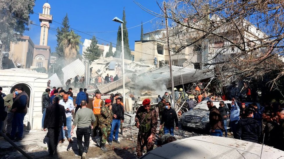 People and security forces gather in front of a building destroyed in an explosion in Damascus on Saturday