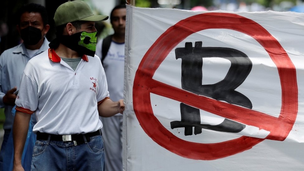 Un hombre con una bandera rechazando el Bitcoin.
