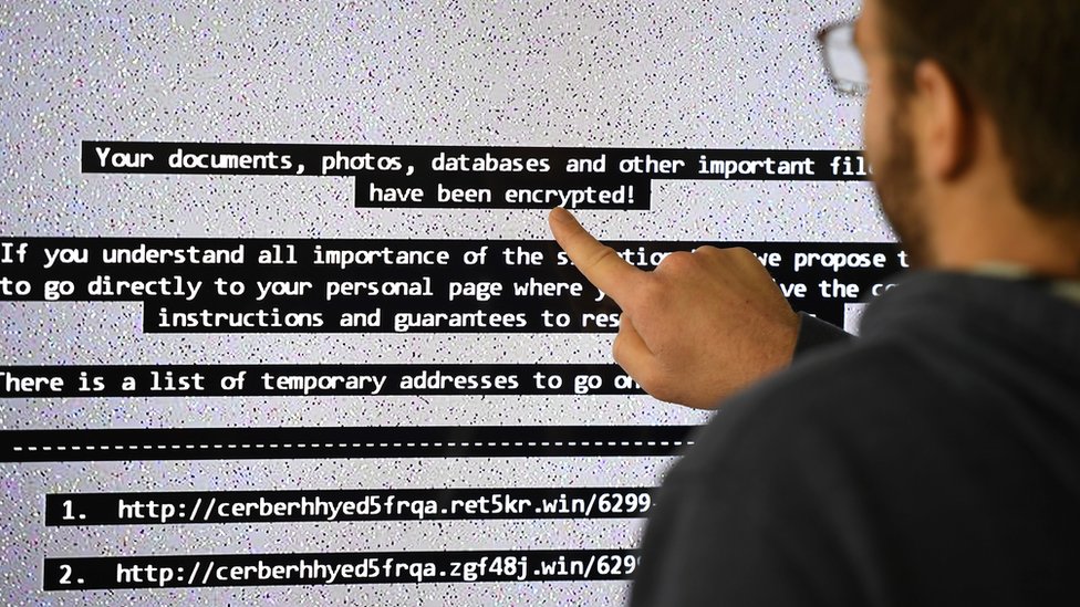 "Sus documentos fueron encriptados", dicen algunos de los mensajes de la amenaza cibernética. hombre señala la amenaza en una pantalla.