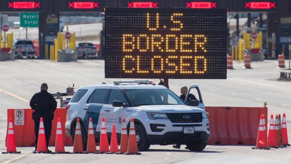 Los funcionarios de aduanas de EE. UU. Junto a un cartel que dice que la frontera de EE. UU. Está cerrada el 22 de marzo de 2020