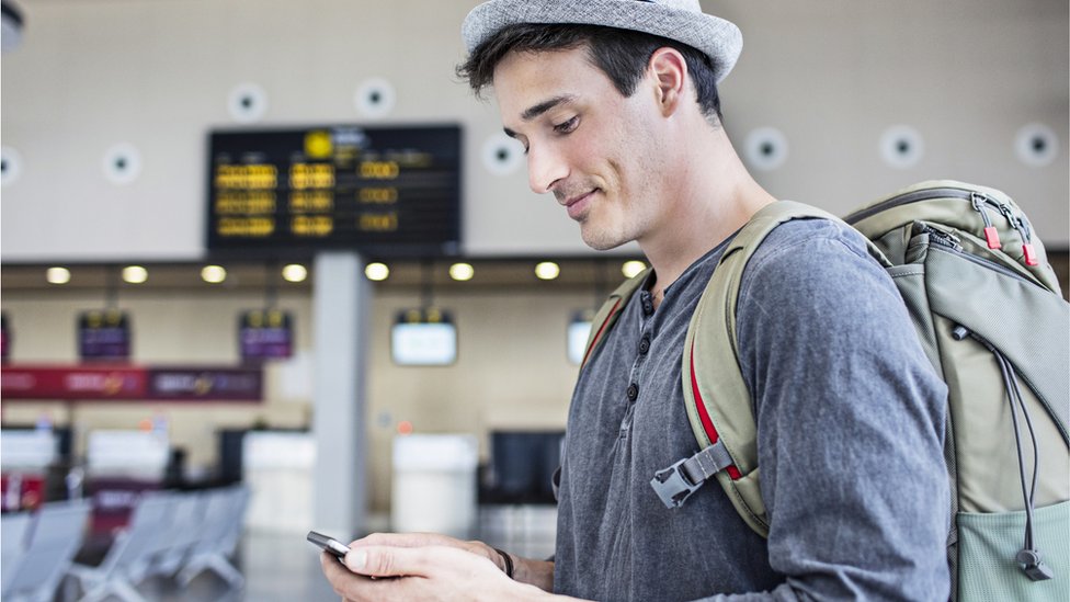 Cargar el teléfono en el aeropuerto no siempre es la mejor opción. Te contamos cuáles son los riesgos. hombre usando teléfono móvil en el aeropuerto.
