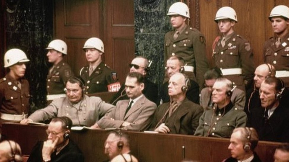 A group of Nazi defendants in court, surrounded by police