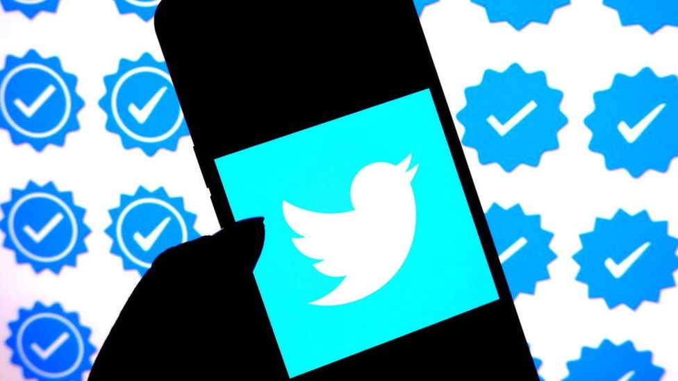Twitter logo displayed on smartphone with blue verification badge symbols in background