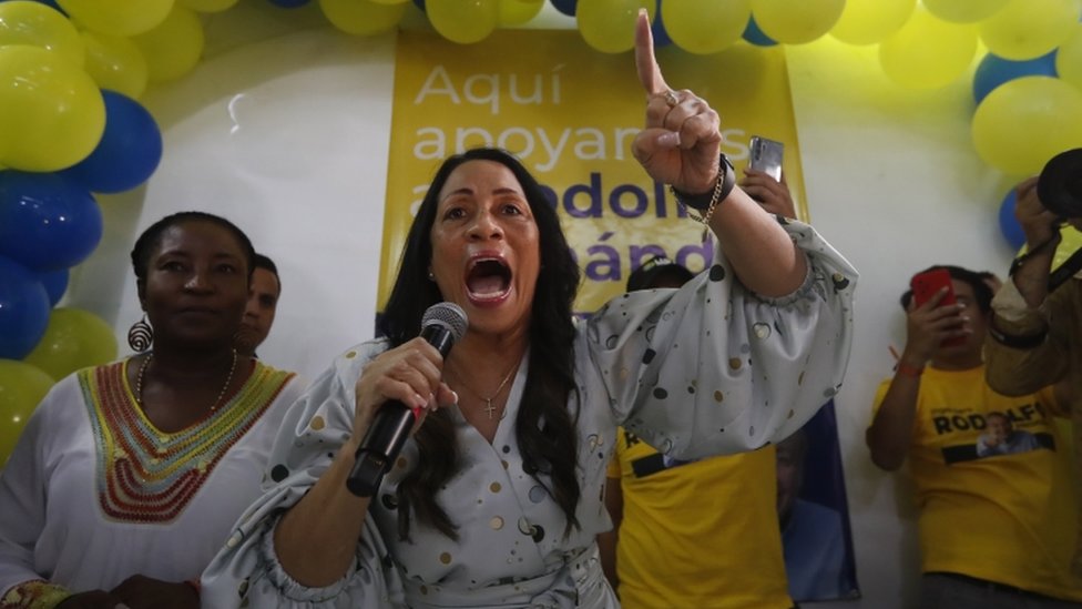 Castillo discursa no microfone e gesticula, observada por outras pessoas