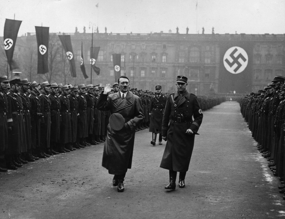 Адольф Гитлер проходит мимо двух рядов гвардейцев перед огромной свастикой на параде в Люстгартене в Берлине в 1936 году