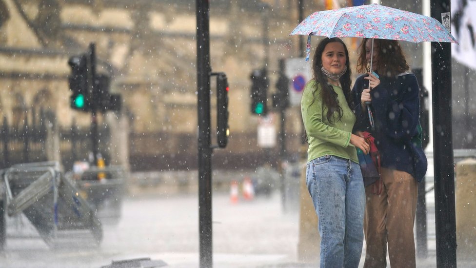 倫敦西敏寺議會廣場上兩位女士瑟縮在一把雨傘下（25/7/2021）