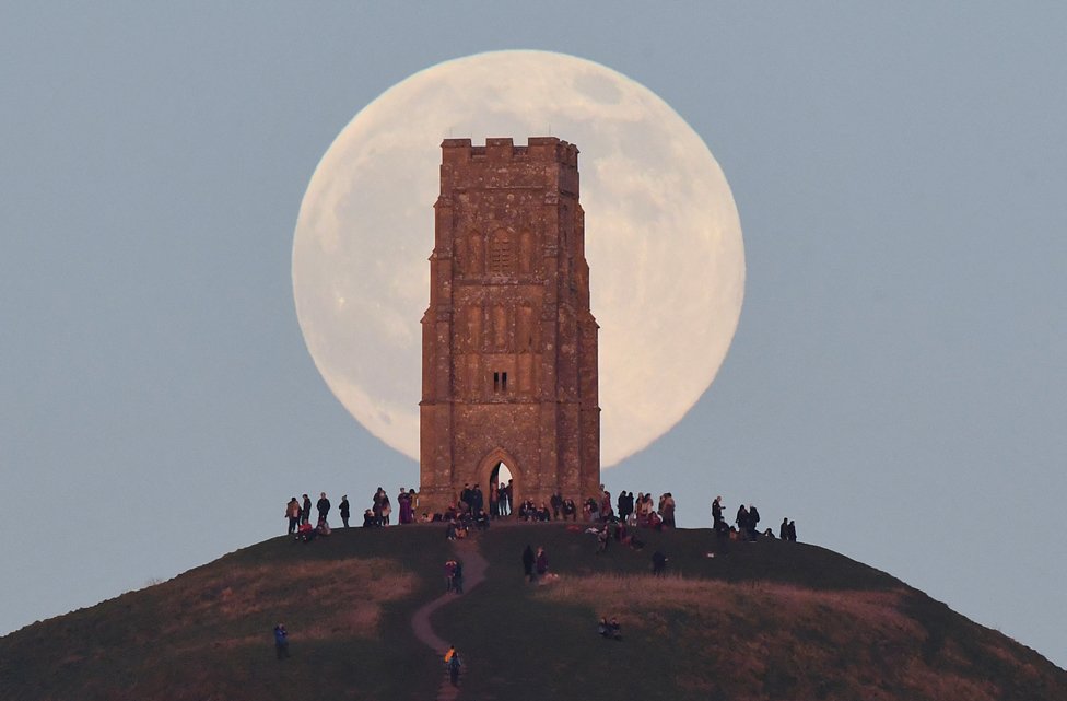 İnsanlar İngiltere'de Glastonbury Tor tepesindeki Aziz Michael kulesinin arkasından ayın doğuşunu izledi