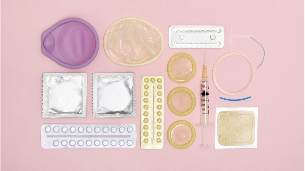 A photo of different forms of contraception on a pink background.