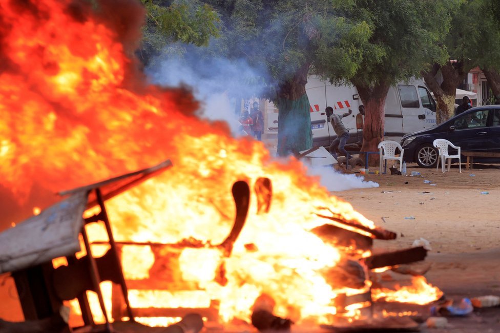 رجل يلقي الحجارة بالقرب من الأجسام المحترقة خلال اشتباكات بين قوات الأمن وأنصار زعيم المعارضة السنغالية عثمان سونكو في داكار، السنغال - الاثنين 29 مايو/ أيار 2023