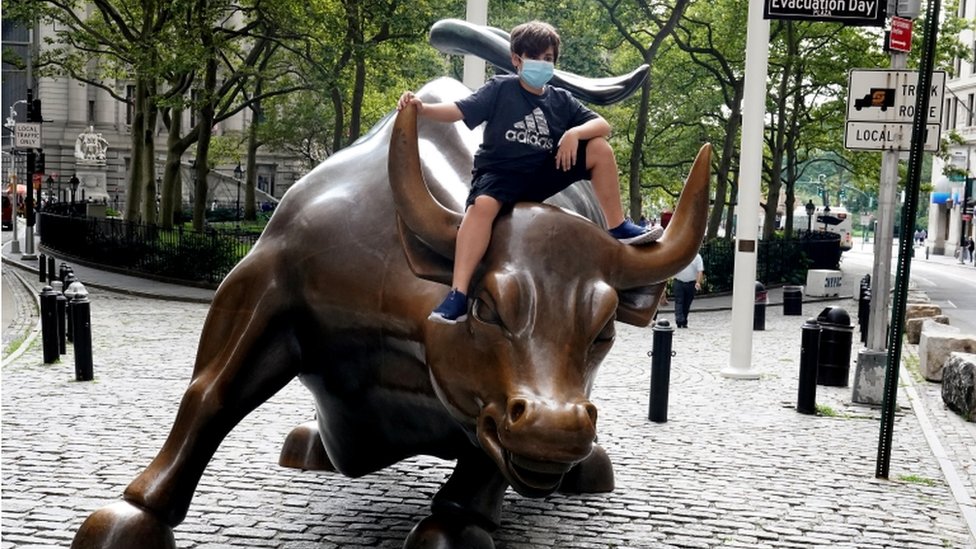 A child wearing a face mask sits on the Charging Bull statue, also known as the Wall St. Bull, following the outbreak of the coronavirus disease (COVID-19) in the Manhattan borough of New York City, New York, U.S., August 19, 2020