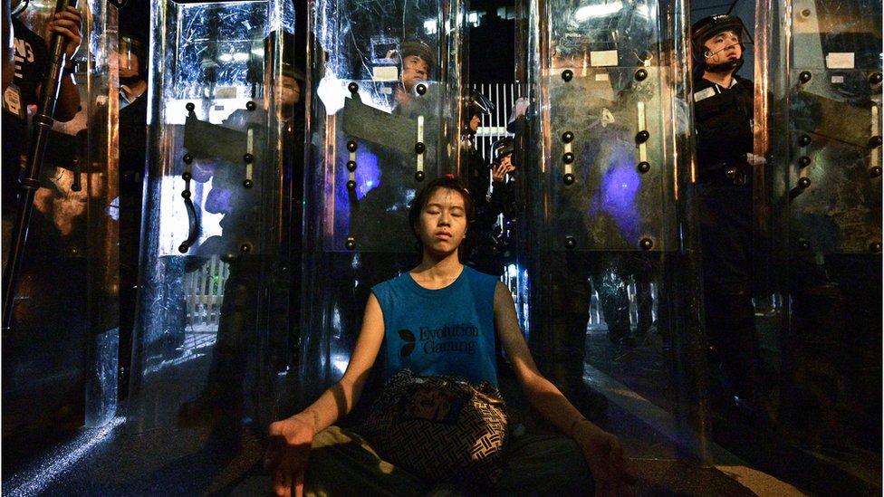 Una mujer medita frente a policías que defienden uno de los edificios de gobierno en Hong Kong