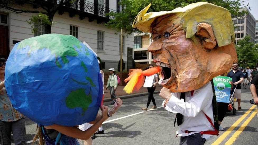Personas con disfraces de la Tierra y Trump peleando.