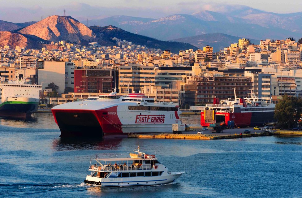 Panoramic view of Piraeus, Greece at sunset showing small and large ferries and mountains in the background