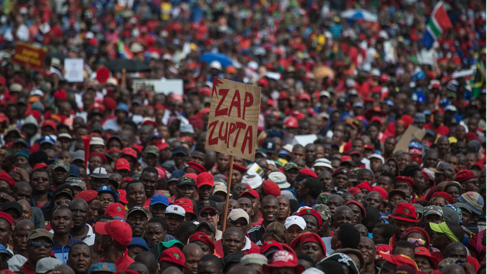 Протестующий держит плакат с надписью «Zap Zupta», относящийся к Зуме и семье Гупта, когда южноафриканские демонстранты из различных политических групп и групп гражданского общества проходят маршем по столице Претории, призывая президента Джейкоба Зуму уйти в отставку 12 апреля 2017 года. || |