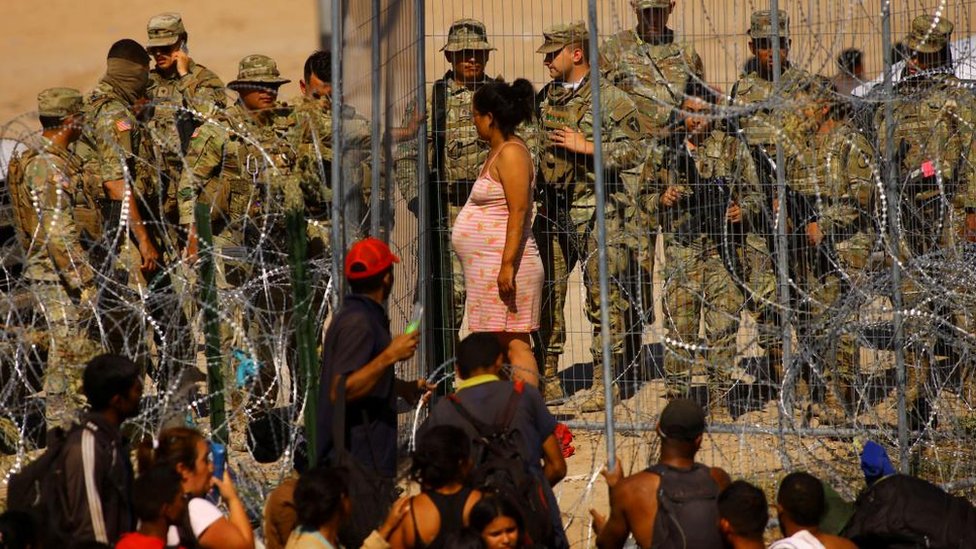 A pregnant woman stands at a security fence installed by the Texas National Guard at the US border with Mexico