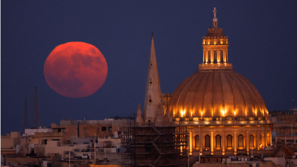 Kızıla dönen rengiyle dolunay, Malta Valetta'daki St. Paul Pro Katedrali ve Our Lady of Mount Carmel Bazilikası'nın ardından görünüyor
