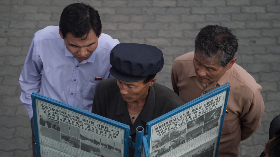 Tres hombres leen un periódico en Pyongyang.