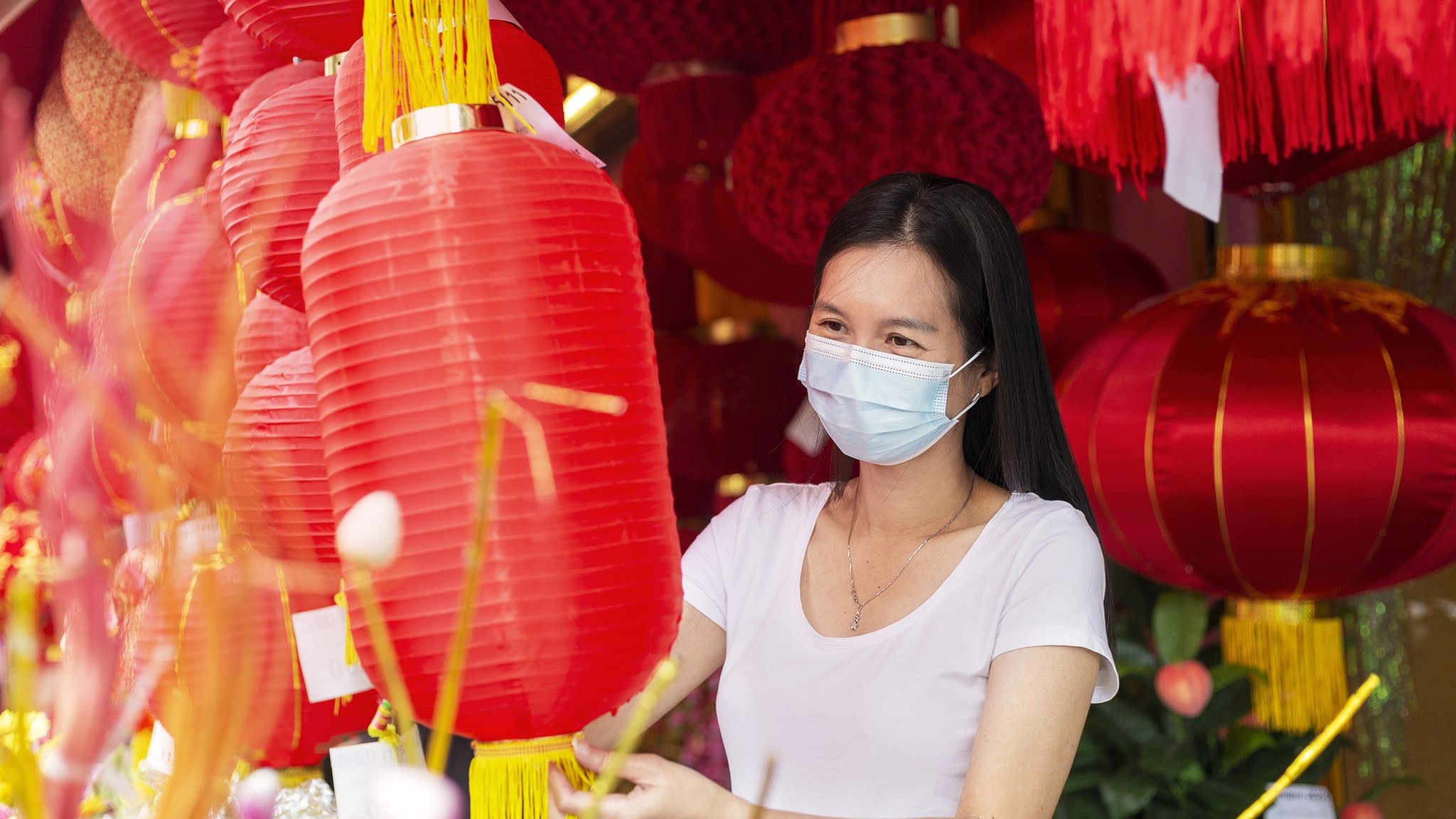 一名戴口罩女子在市場上挑選傳統的紅燈籠，為在農曆新年期間裝飾自己的家做凖備
