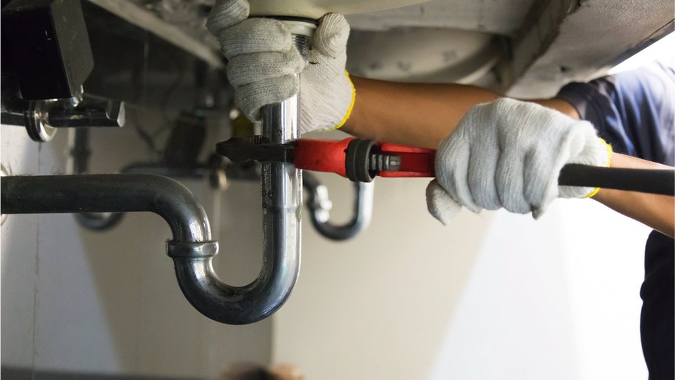 Plumber fixing white sink pipe with an adjustable wrench