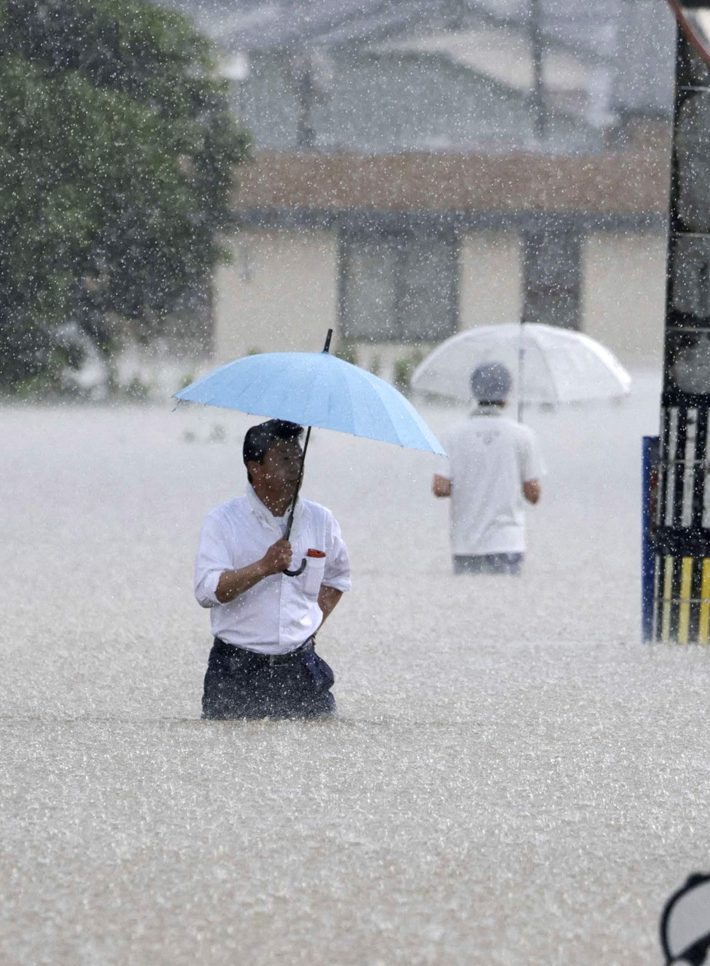 ​​People make their way in a flooded road in heavy rain in Kurume, Fukuoka Prefecture, Japan - 10 July 2023