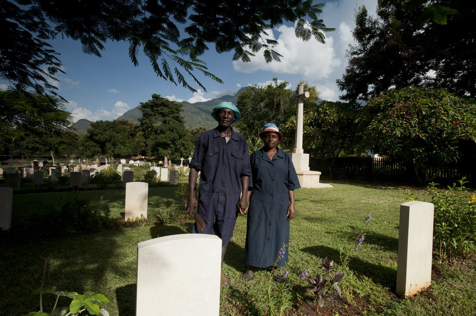 Шадрак Паулл и Лусия Аксальте стоят, держась за руки среди могил на кладбище в Танзании