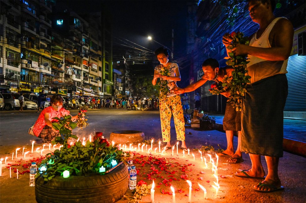 People lay flowers around a circle of candles on a street