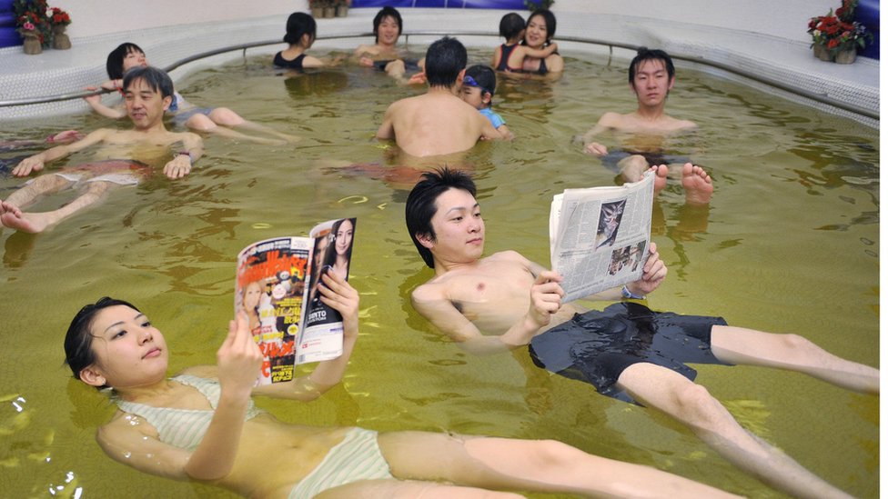 Два японца читают журнал и газету, плавая в «спа мертвого моря»