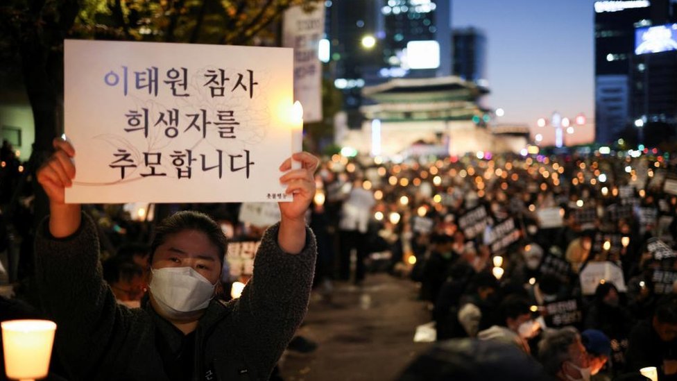 首爾廣場一場悼念梨太院踩踏事件的燭光晚會上一位女士舉起悼念標語（5/11/2022）