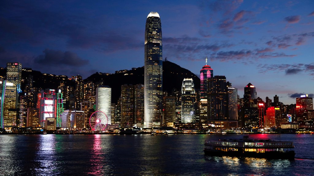 Victoria Harbour in front of a skyline of buildings in Hong Kong with mountains behind them