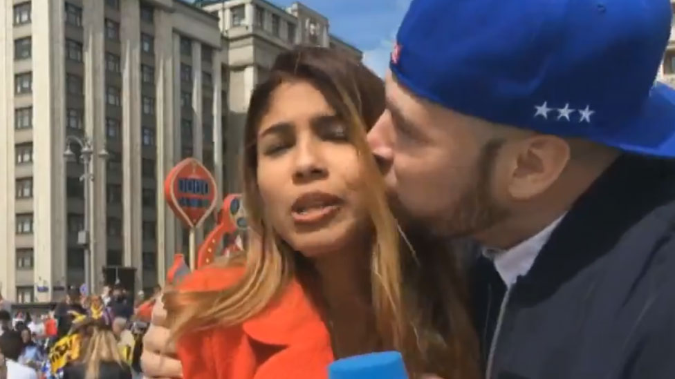Un fanático de fútbol besa a una periodista que se la ve claramente incómodo mientras sostiene un micrófono DW.